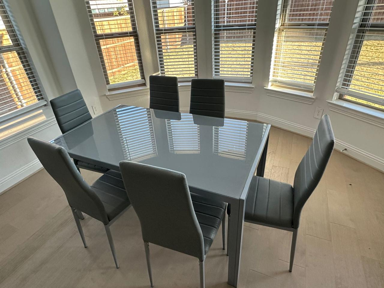 Grey glass-top dining table with 6 chairs in bay window